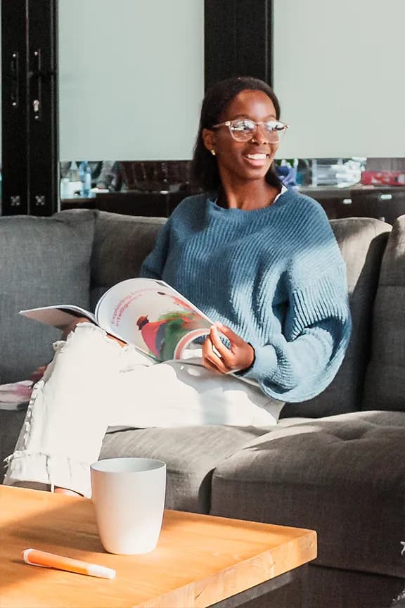 A woman sitting on a couch, engaged in reading a book, with a coffee cup on the nearby table.