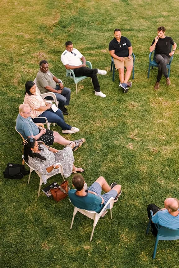 Group members sitting in a circle on chairs on grass.