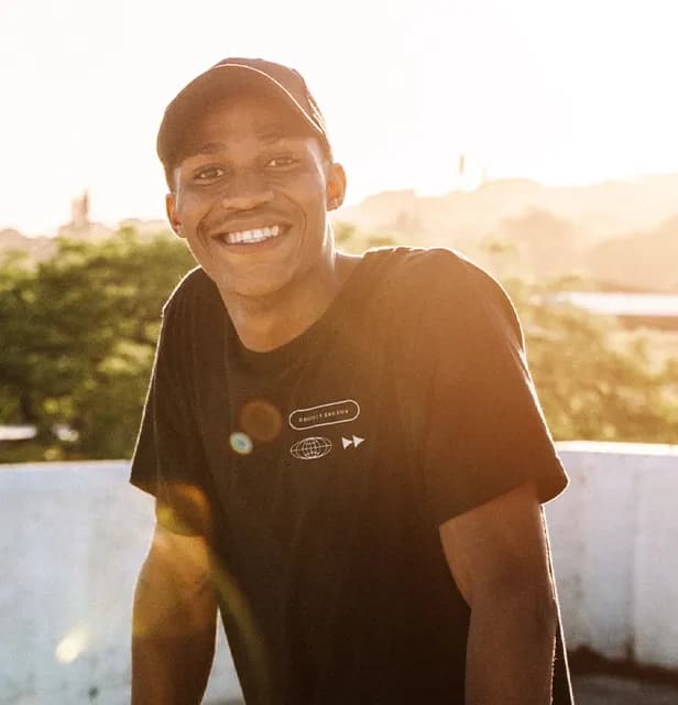 A smiling man wearing a hat in warm sunlight.