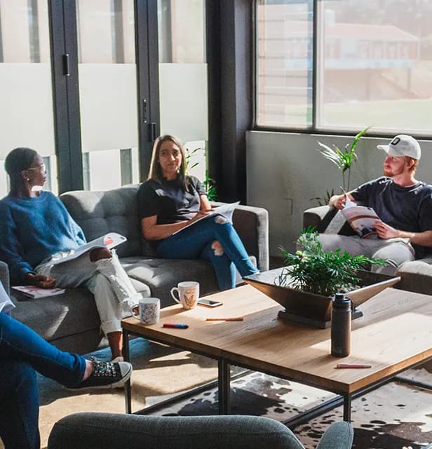 A small group of people seated on couches with workbooks in a lounge setting.
