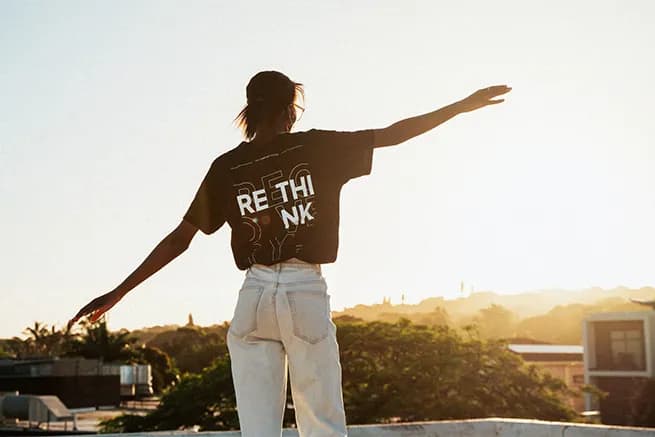 Woman on a rooftop at sunset, arms outstretched.